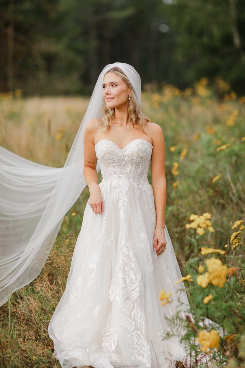 Bride in lace wedding dress standing in a lush, flower-filled field near Minocqua, WI.