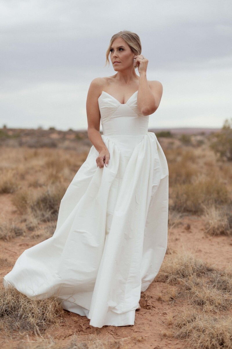 Bride in a white wedding gown standing in desert landscape.