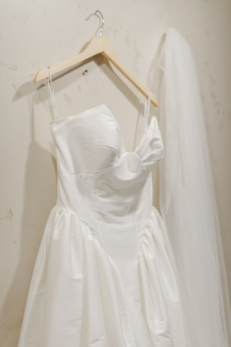 White wedding dress hanging on a wooden hanger.