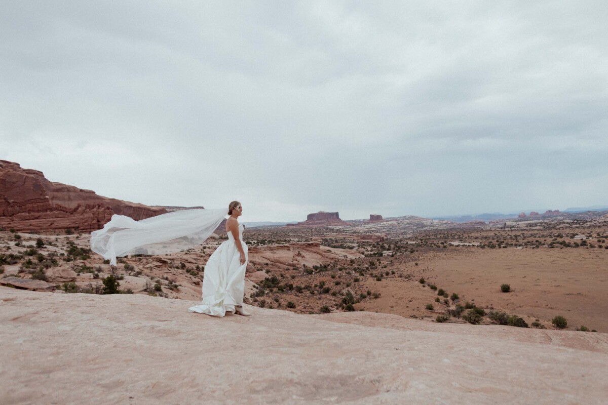 Bride in wedding dress with flowing veil in Moab Utah landscape.
