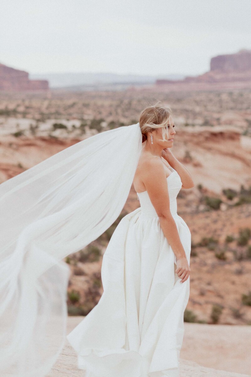 Bride in a white wedding dress with flowing veil in Moab Utah landscape.
