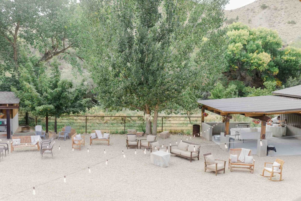 Beautiful outdoor wedding scene with seating area under large trees and mountain backdrop.