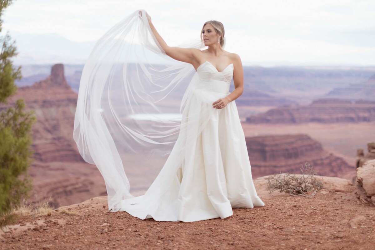 Bride in wedding dress holding veil at Moab Utah with canyon views.