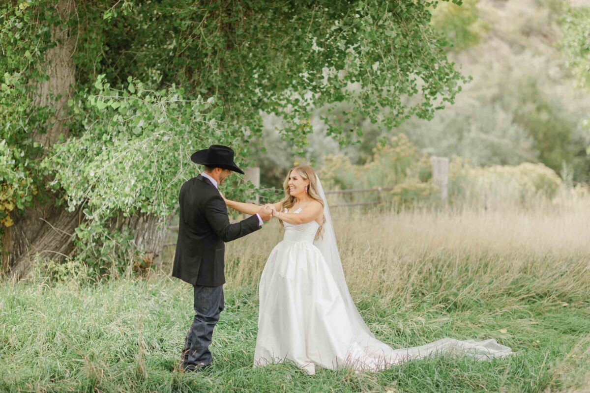 Bride and groom sharing a special moment under a large tree in a rural landscape.