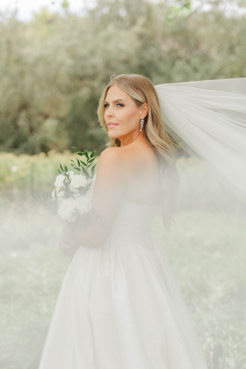 Bride with veil and bouquet in natural setting.