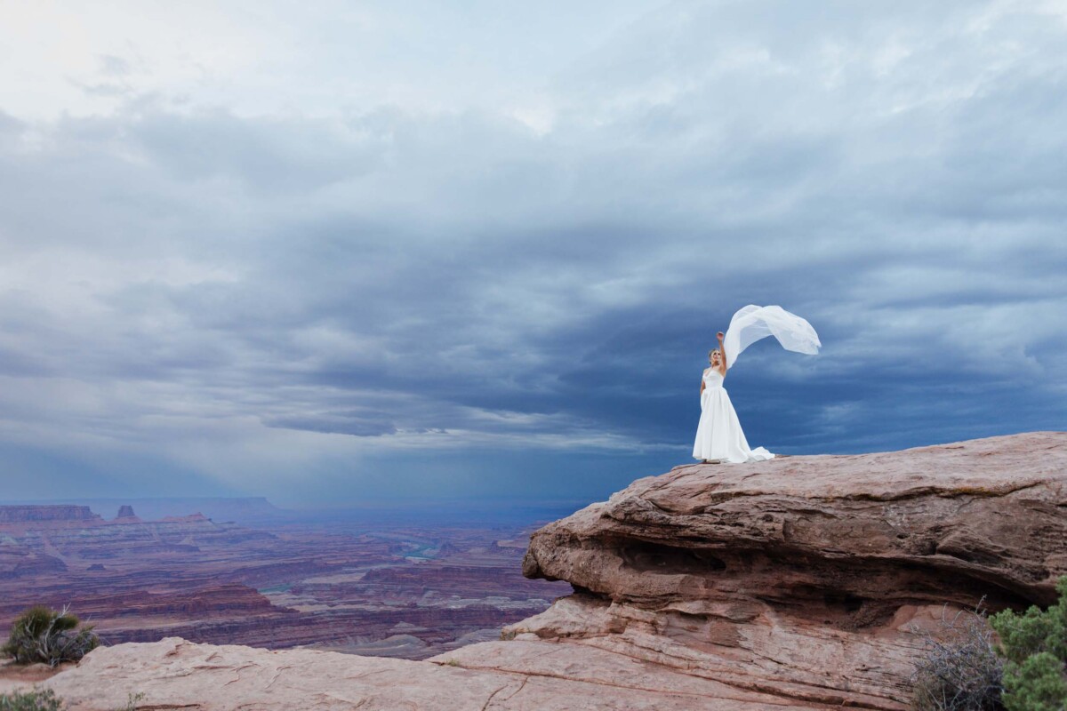 Bride with flowing veil on rock cliff in Moab, Utah.