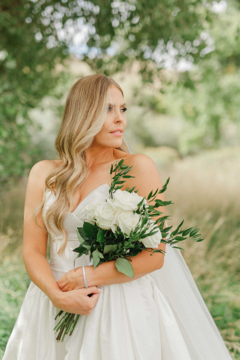 Bride with a bouquet of white roses and greenery outdoors.