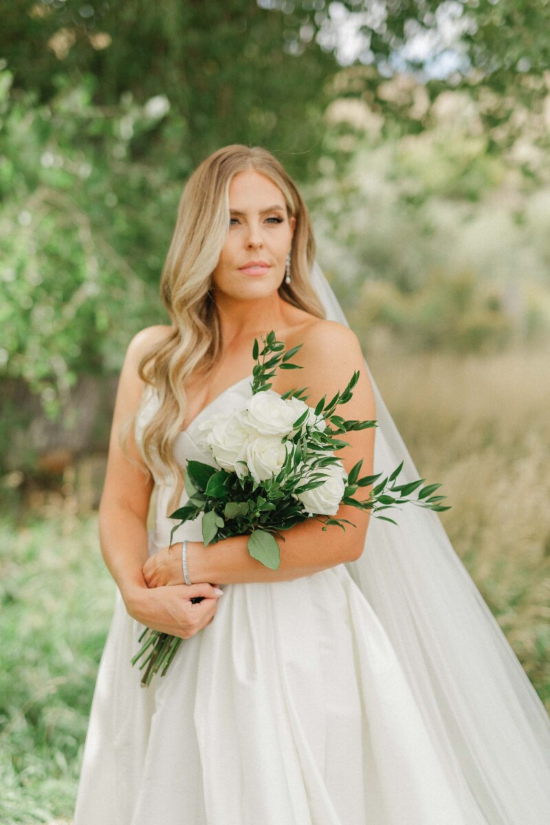 Bride with a white wedding dress and bouquet in a lush green setting.