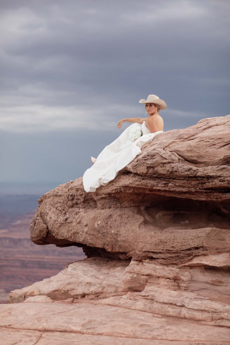 Elegant bride sitting on rock formation in Moab, Utah.
