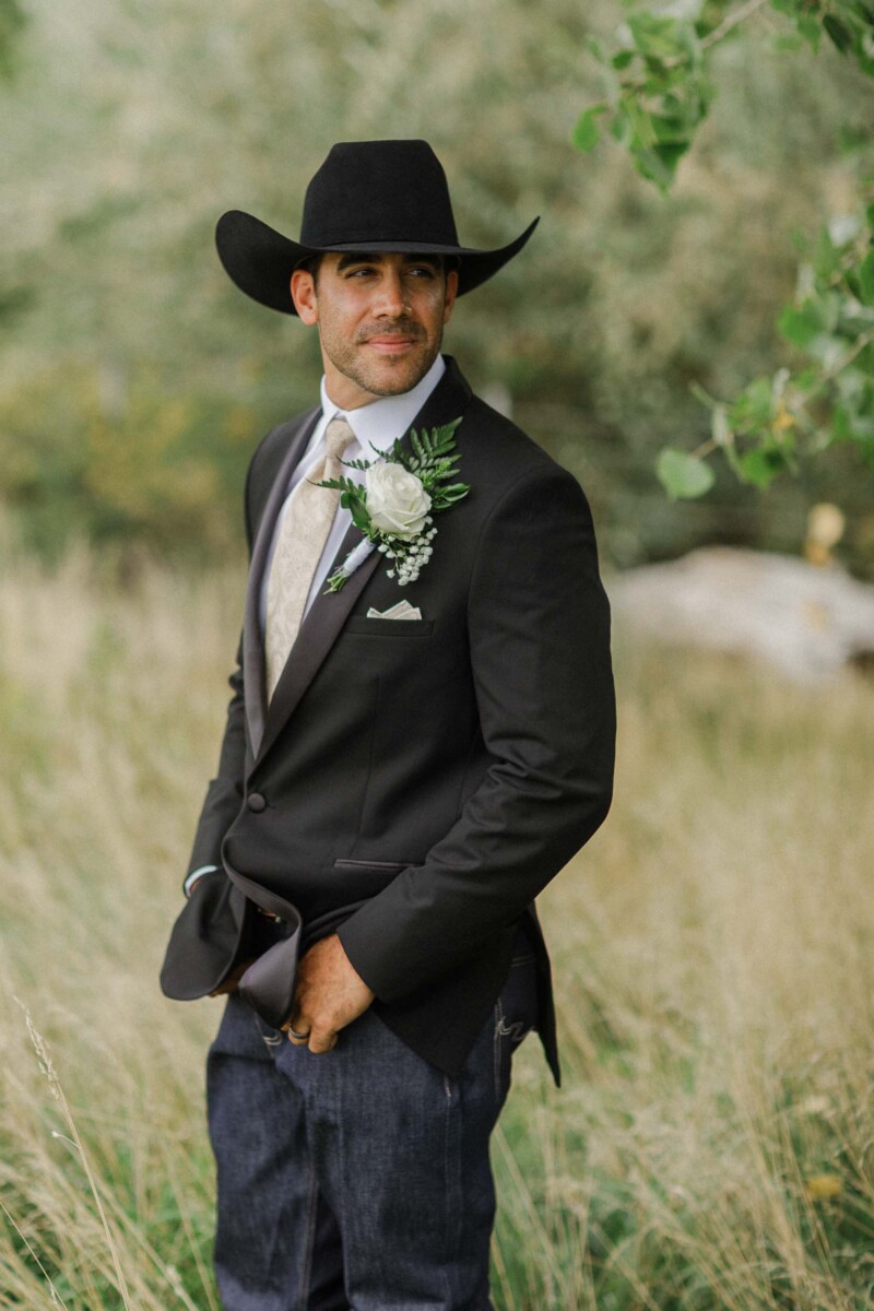 Groom in cowboy hat and suit outdoors during rustic Utah wedding.