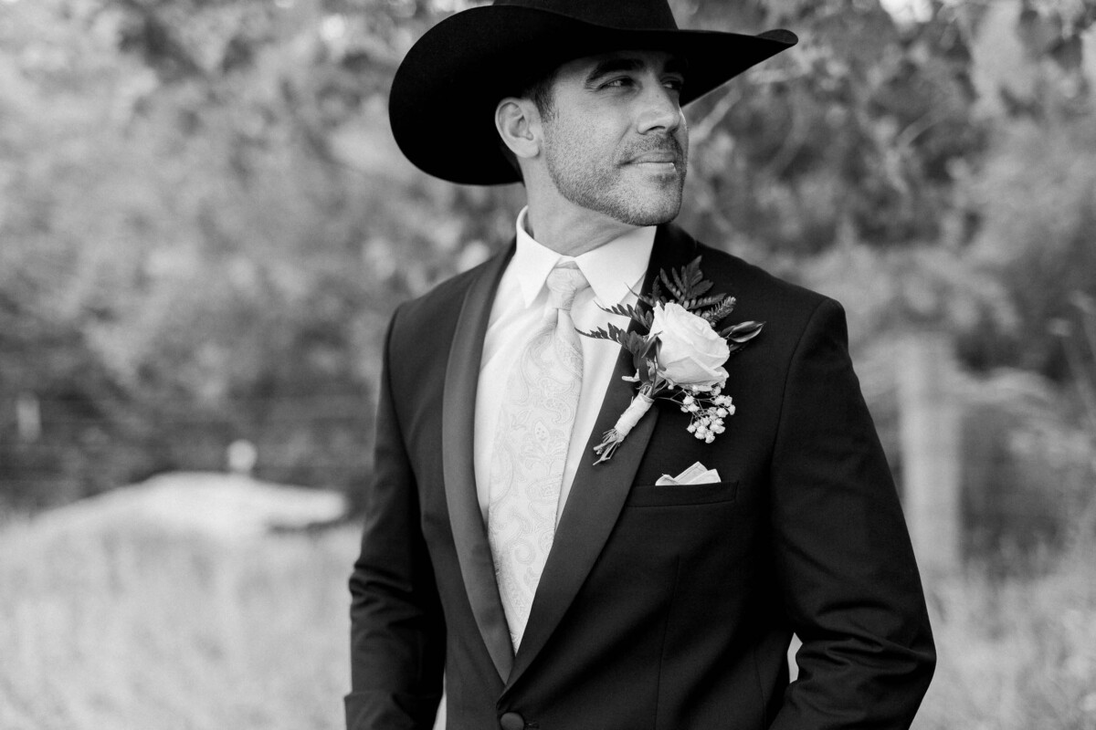 Groom in black suit and cowboy hat at rustic outdoor wedding in Utah.