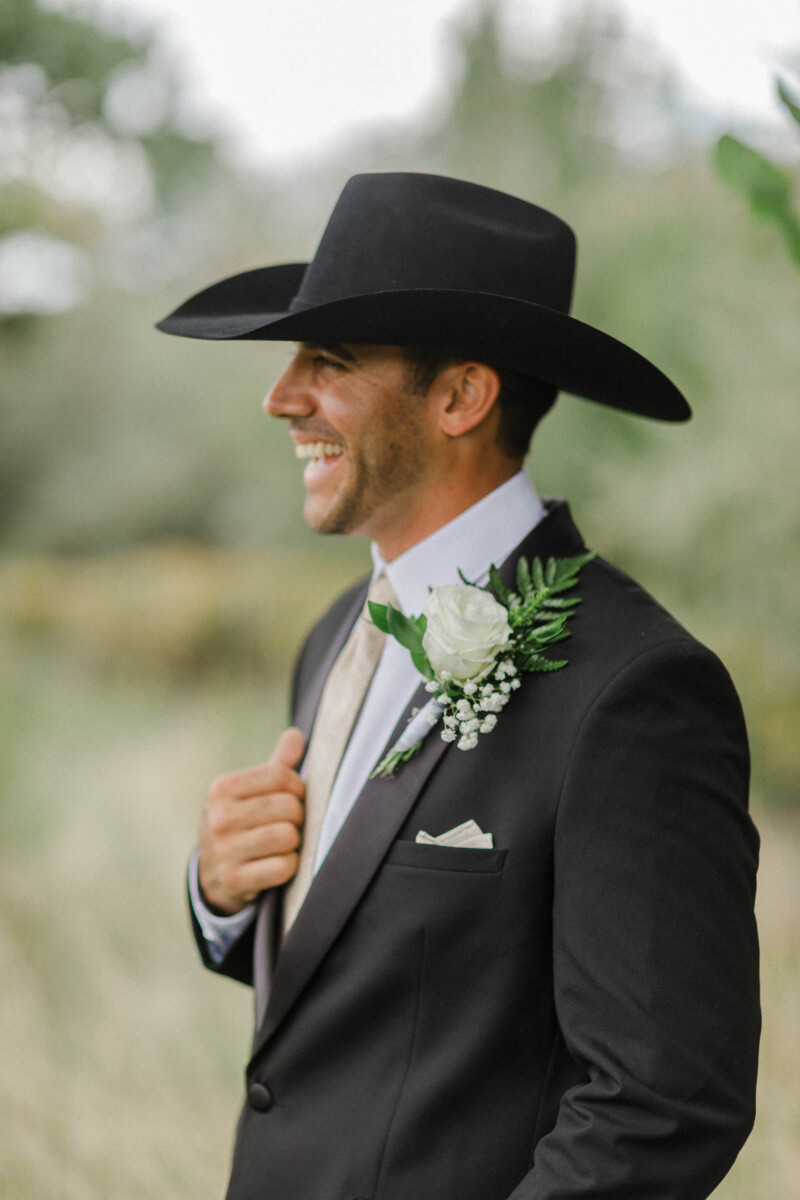 Groom in a black suit and hat smiling outdoors during a Utah fall wedding.