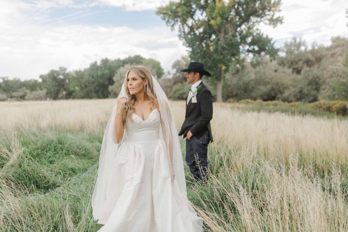 Bride in a white gown with veil, groom in black suit and cowboy hat.