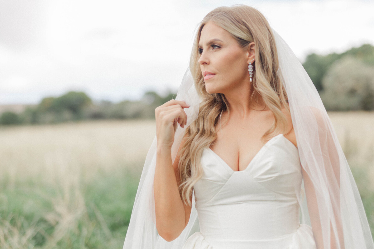 Bride in a white wedding dress with veil outdoors in a rural setting.
