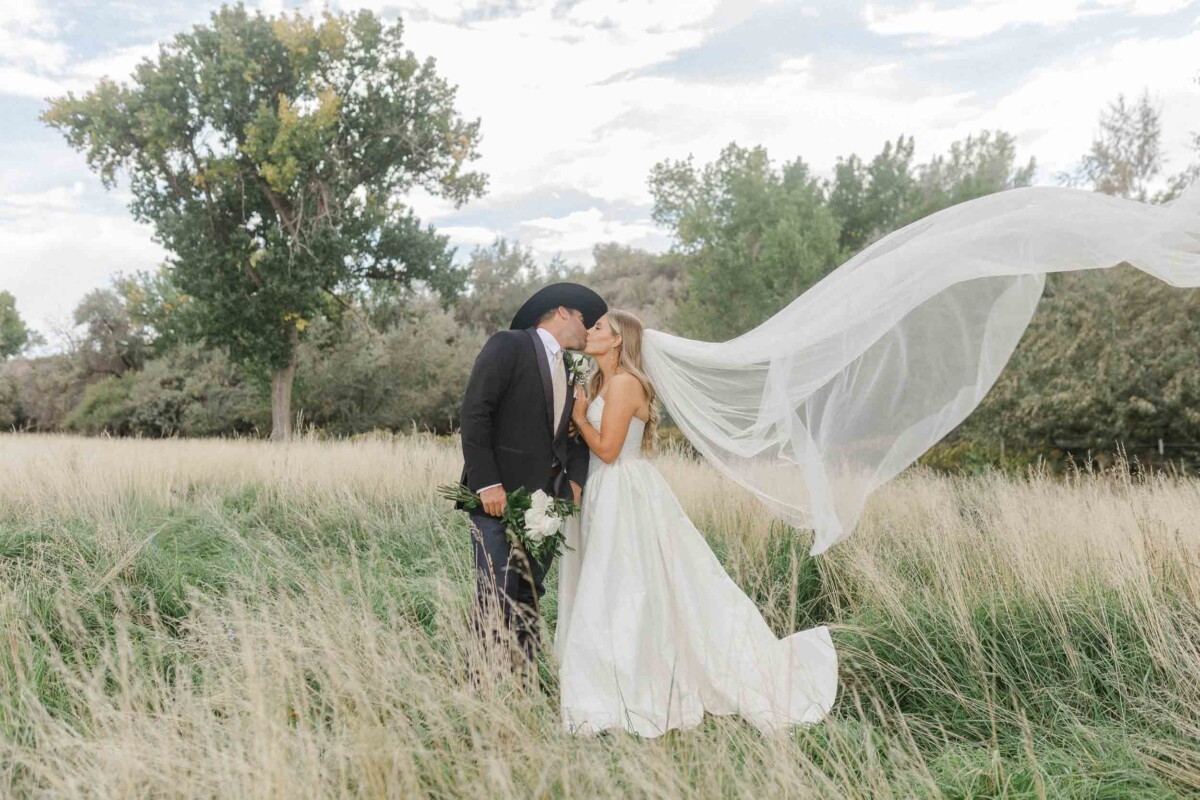 Romantic wedding photo of couple kissing outdoors with flowing veil in a rural Utah landscape.