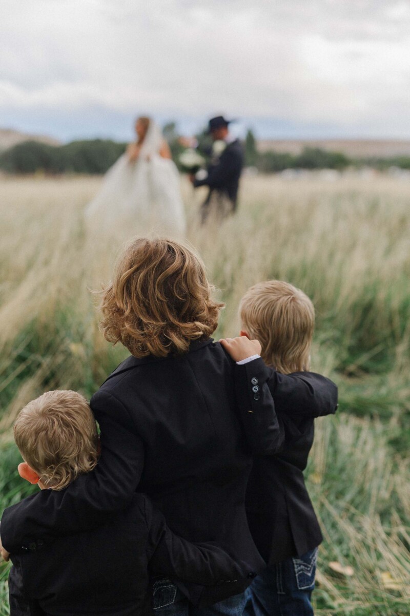 Family watching wedding in a field with a bride and groom in the background.