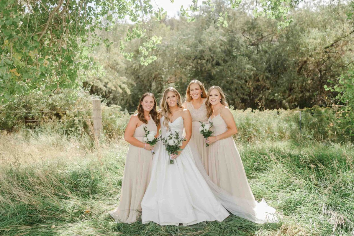 Beautiful wedding photo of bride and bridesmaids in a lush outdoor setting.