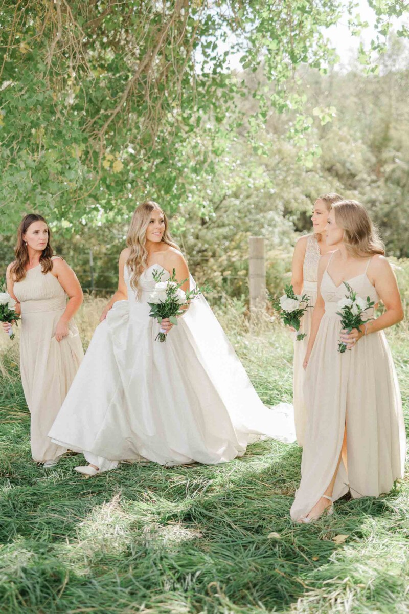 Elegant wedding photo of bride and bridesmaids outdoors in lush greenery.