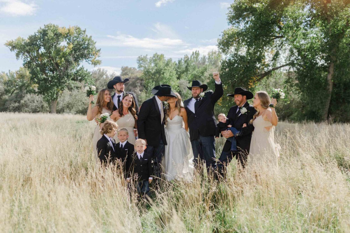 Wedding party celebrating outdoors in a scenic field with trees and blue sky.