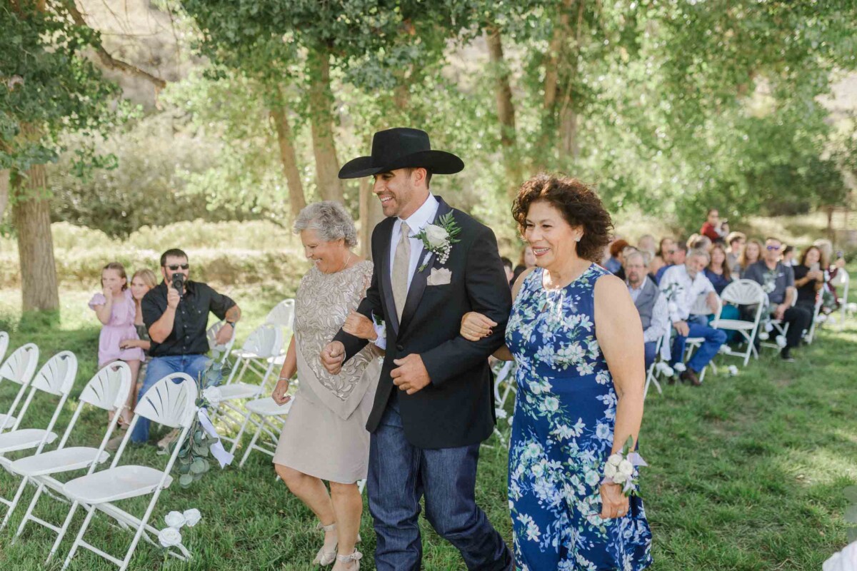 Elegant wedding procession outdoors with guests seated on white chairs.