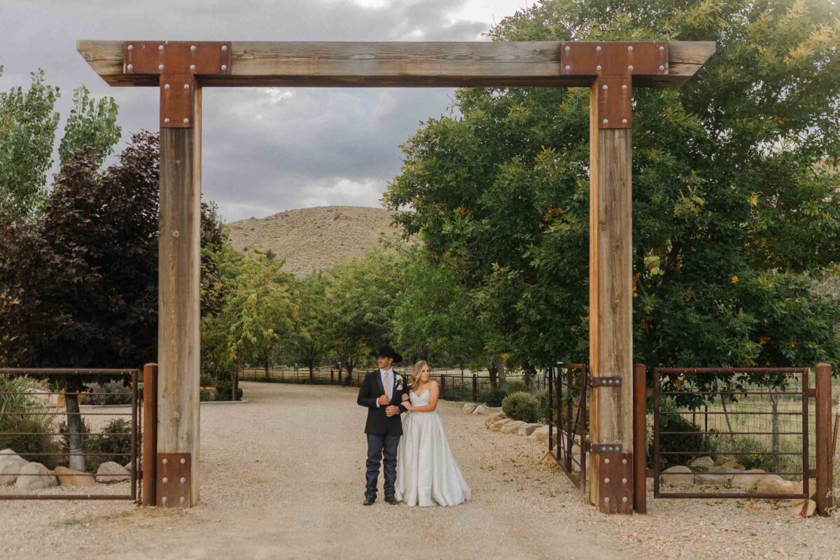 Beautiful couple standing under rustic wooden archway in rural Utah setting.