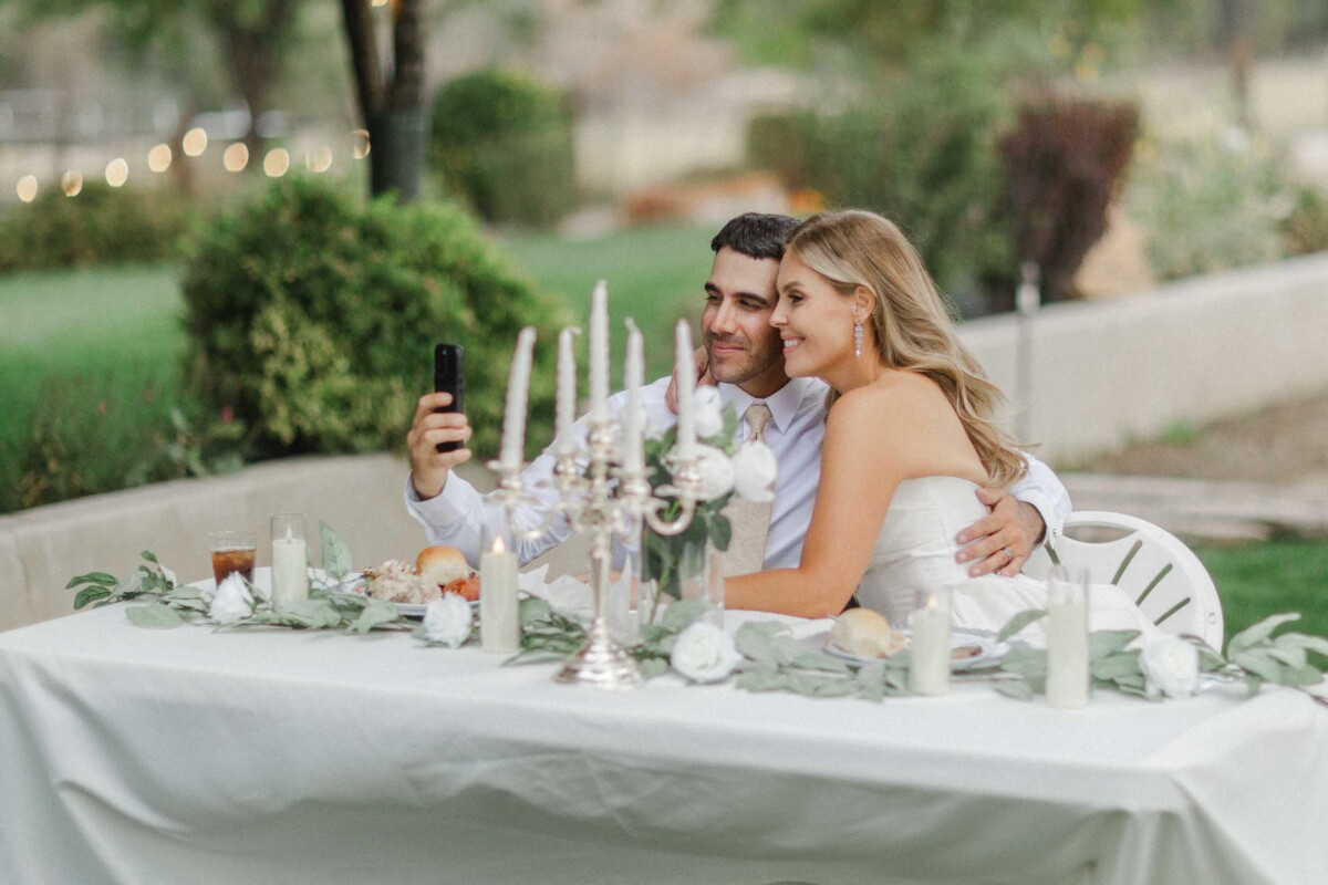 Happy couple taking a selfie at their rustic outdoor wedding reception.
