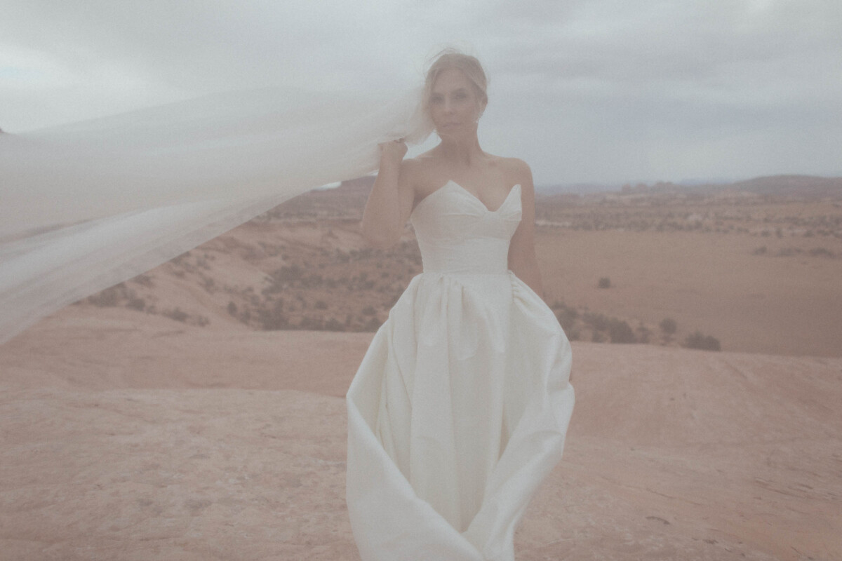 Elegant bride in a flowing white gown with desert landscape background.