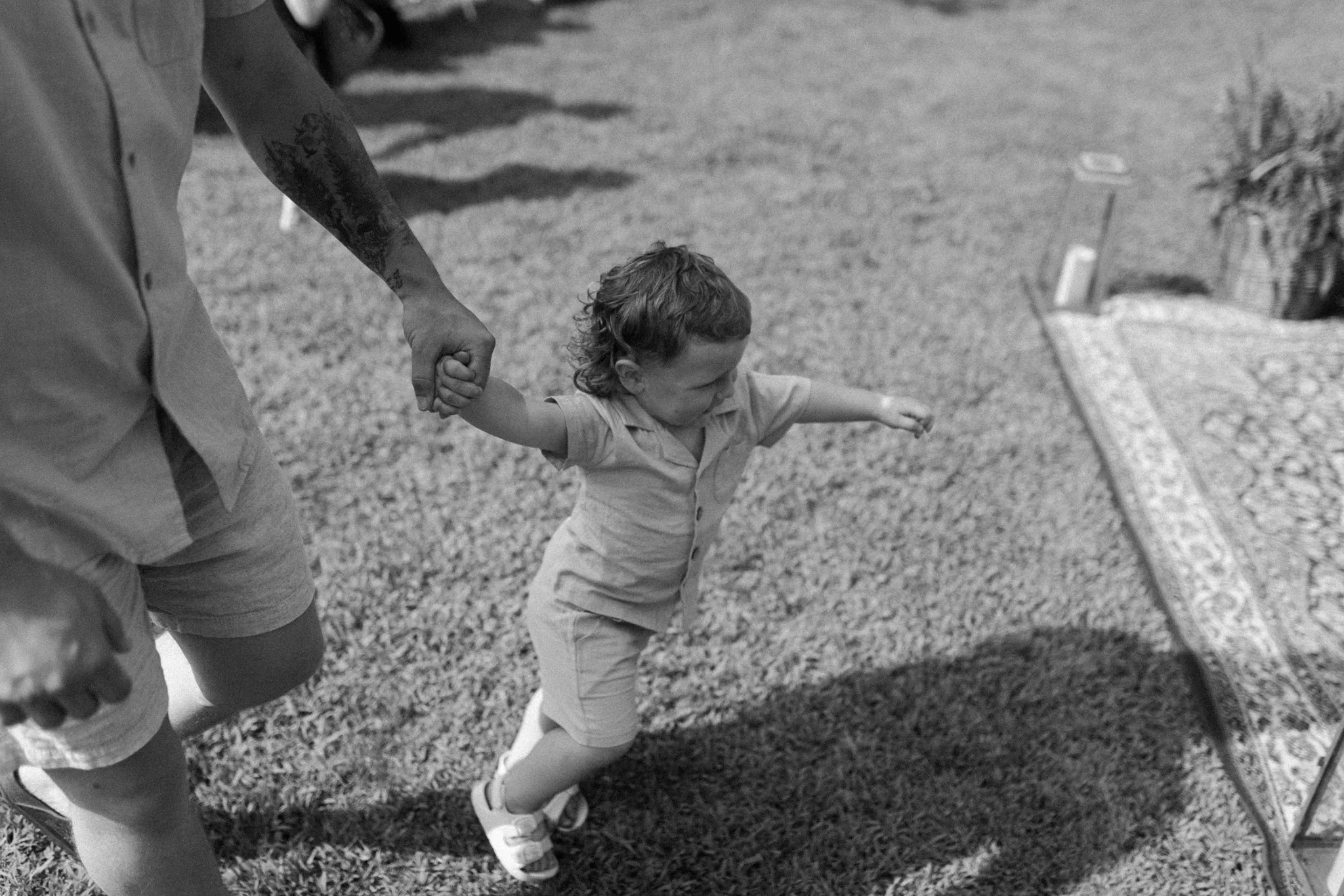 Black and white documentary photo of toddler being guided by hand at Wisconsin Dells backyard wedding ceremony