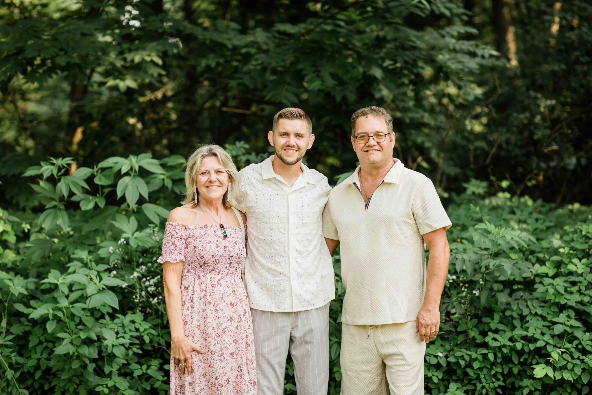 Groom with parents in front of lush green trees at Wisconsin Dells backyard summer wedding