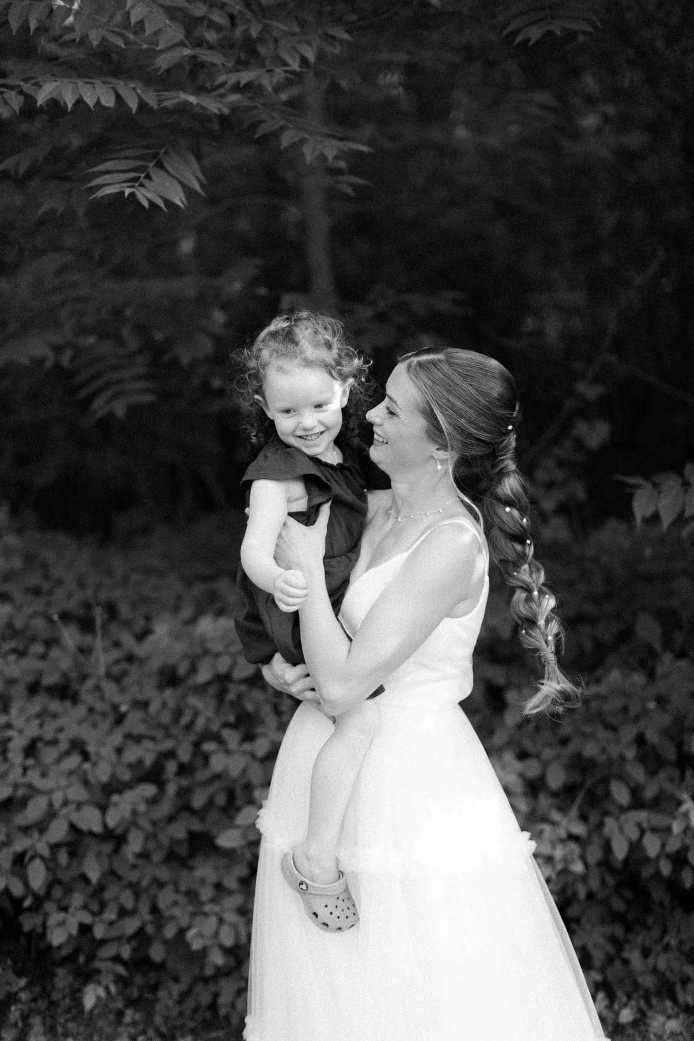 Black and white documentary photo of bride holding young child at Wisconsin Dells backyard wedding