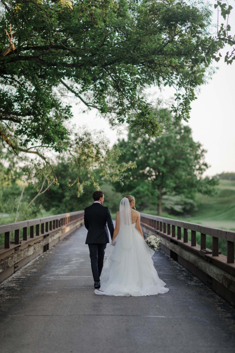 Bride and groom walking a tree-lined bridge over the grounds at Destination Kohler, a Straits Chapel wedding by James Stokes and Co