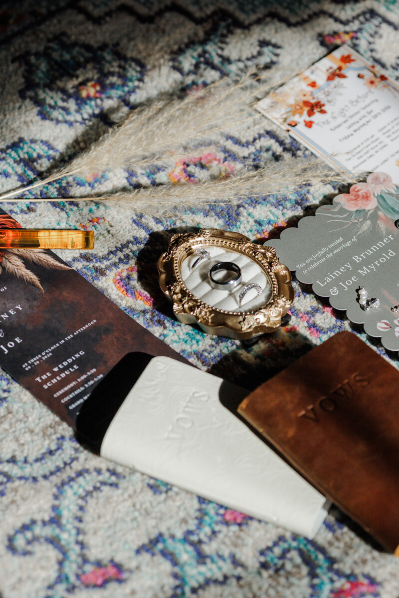 Wedding rings in an ornate gold ring box beside leather vow books and the invitation suite