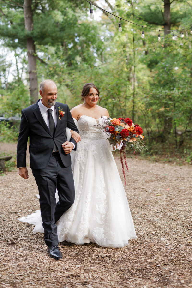 Father walking the bride down the aisle through the forest ceremony site