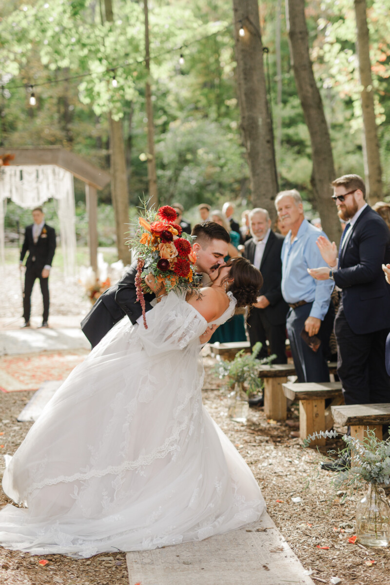 Groom dipping the bride for a kiss in the aisle as guests cheer