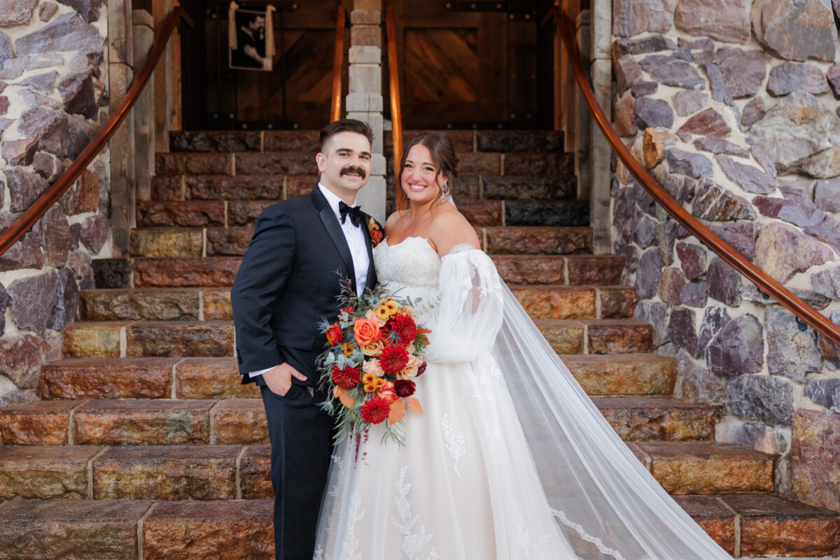 Bride and groom smiling on the stone stairway at The Swan Barn Door
