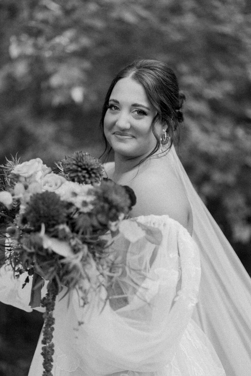 Black and white portrait of the bride smiling over her bouquet