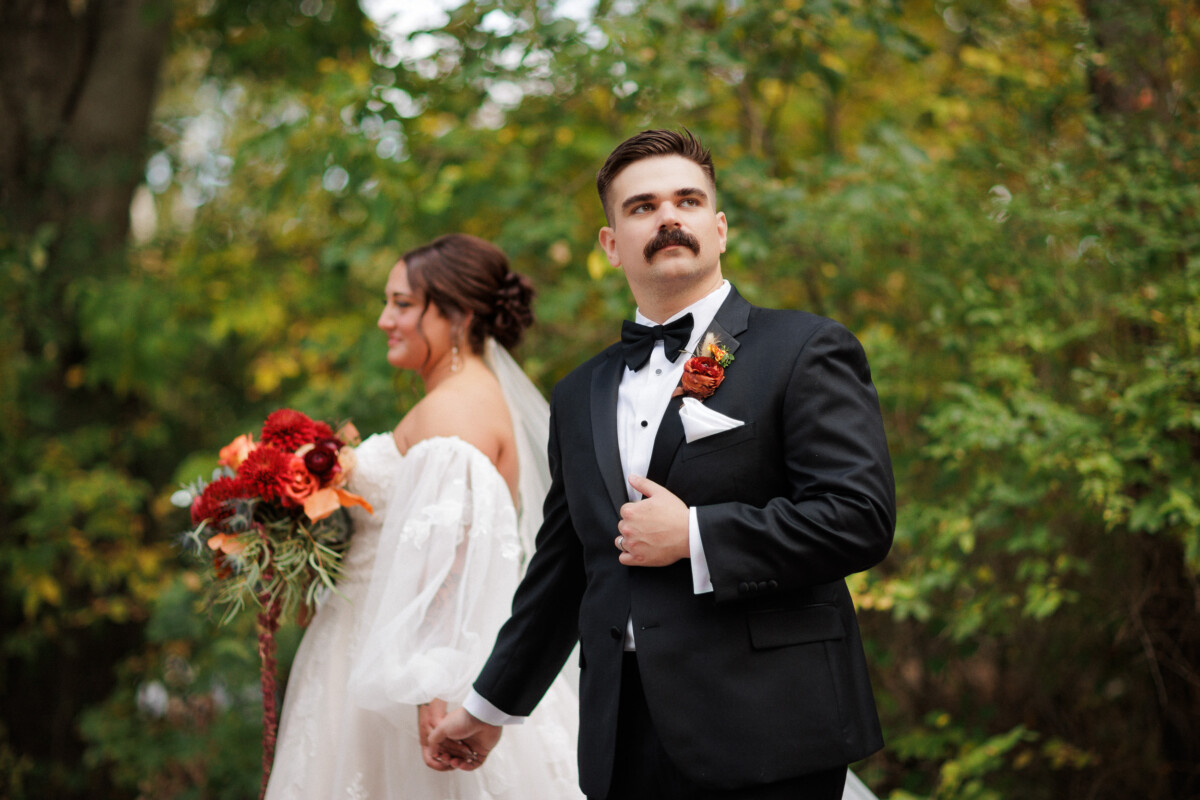 Groom smiling as he leads the bride through the trees