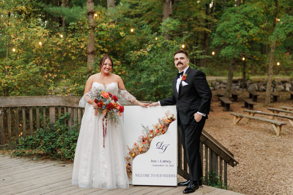 Bride and groom smiling beside their welcome sign in evening light