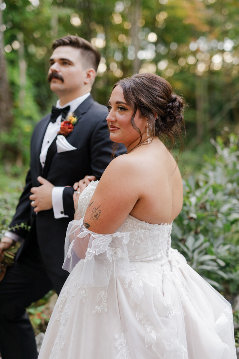 Bride and groom standing close among green trees in evening light