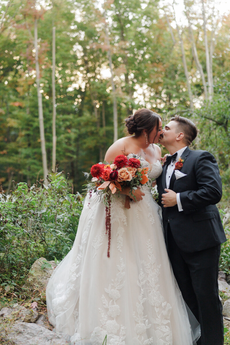 Bride and groom embracing among tall trees at sunset