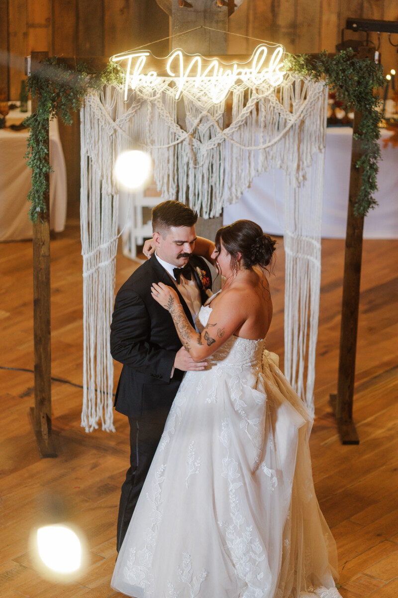 First dance beneath the neon sign and macramé backdrop inside the barn